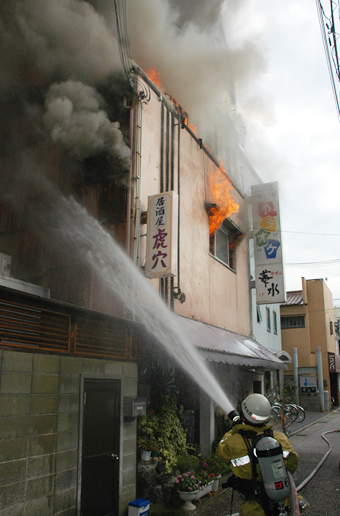 窓から炎を出して燃える建物に放水する消防隊員