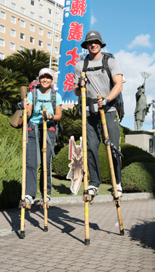 竹馬で日本縦断に挑戦中のマイケル・タンさんと実希さん夫妻。リュックにつけたオランウータンのぬいぐるみが募金を呼びかけるボードを持っている