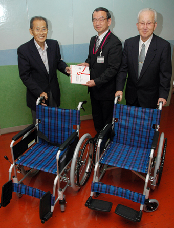中山茂雄理事長(左)に車いすを贈る青木繁店長と専門店会の井口浅夫会長(右)
