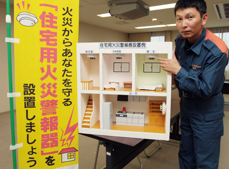 家屋の断面模型を使って火災警報器の設置場所を説明する消防署員