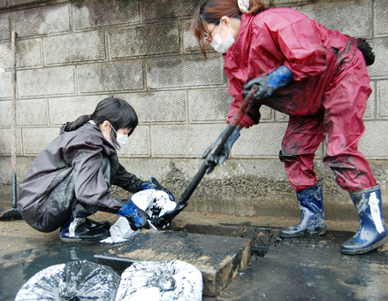 被災地の側溝で泥の除去を行う学生ボランティア＝大学提供