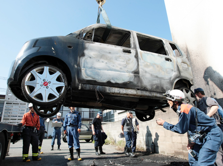 原因不明の出火で全焼した軽自動車を検証する捜査関係者