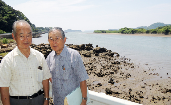 「日野七族」が上陸したと伝えられる相浦川河口部を案内する田渕信幸さん(右)と澤正明さん