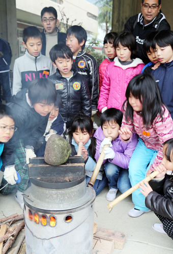 かまど炊き体験で火吹き竹を使って空気を送り込む児童たち