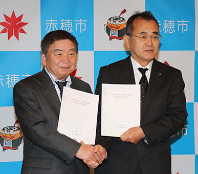 災害時物資供給協定を締結して握手を交わす明石元秀市長と浦上晃之社長(左)