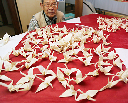 一枚の和紙から折られた連鶴と作者の三木豊さん