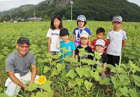 「大輪の花を咲かせて」と木津ひまわりまつり当日の開花を願う溝田泰司会長と農作業サポーターの子どもたち