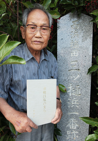 「赤穂は塩のまち」を発刊した長田作一さん=西浜塩田の名残を示す石柱の横で