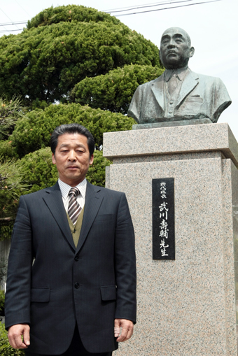 武川壽輔・初代校長像を前に「文武両道の伝統を引き継ぎたい」と語る佐見津和彦校長