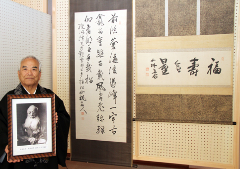 大鳥圭介墨蹟展の展示品と西光寺・多田満之住職。手にしているのは圭介の遺影