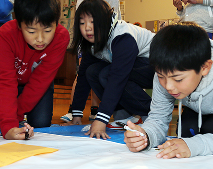 キャンバスの裏面にサインする児童たち