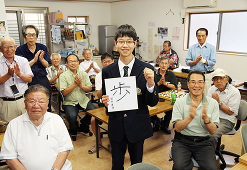 赤穂楽碁会の碁会所でプロ入段を祝福される田中康湧さん=中央。色紙には「一歩ずつ着実に進む」との思いを込めた