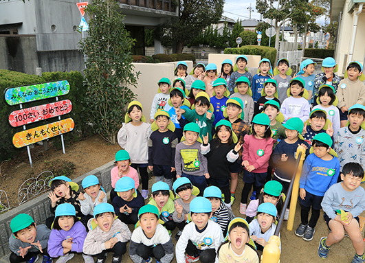 創立１００周年で記念植樹されたキンモクセイの横で「１００歳おめでとう」と祝う園児たち